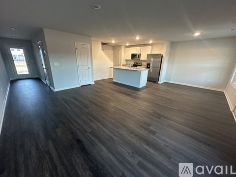 A spacious room with wooden flooring and a kitchen area in the background.