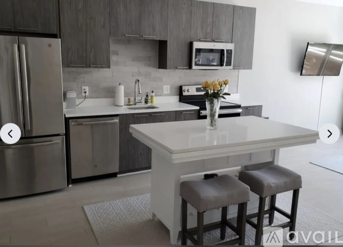 A modern kitchen with a refrigerator, microwave, and a table with two stools.