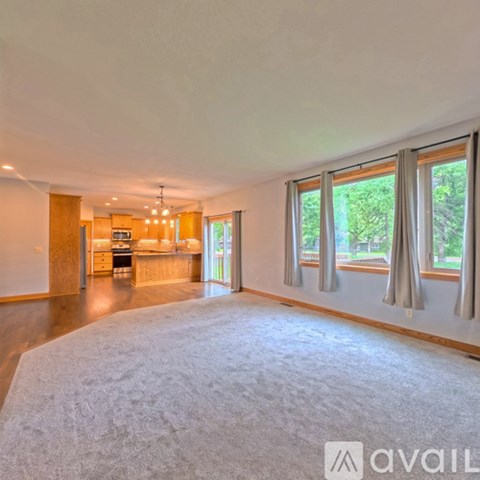 A spacious living room with a grey carpet and a kitchen in the background.