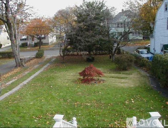 A white fence borders a green lawn with a red bush in the middle.
