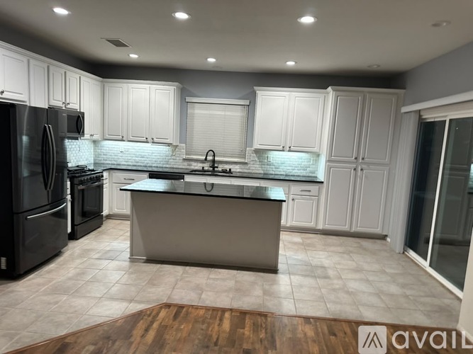 A modern kitchen with a black refrigerator, white cabinets, and a wooden floor.