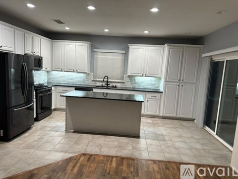 A modern kitchen with a black refrigerator, white cabinets, and a wooden floor.