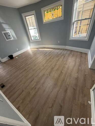 A room with wooden flooring and two windows.