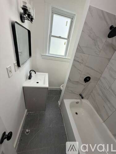 A bathroom with a tub, sink, mirror and window.