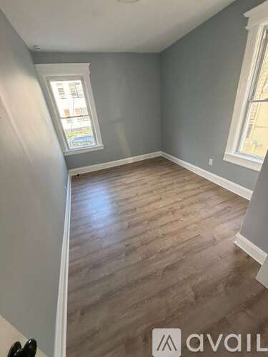 A room with wooden flooring and two windows.