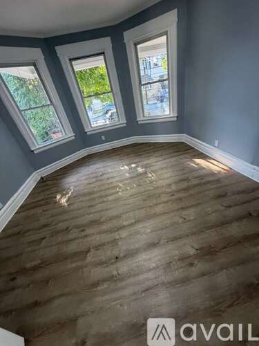 A room with wooden flooring and three windows.