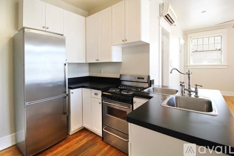 A kitchen with a stainless steel refrigerator, black countertops, and white cabinets.