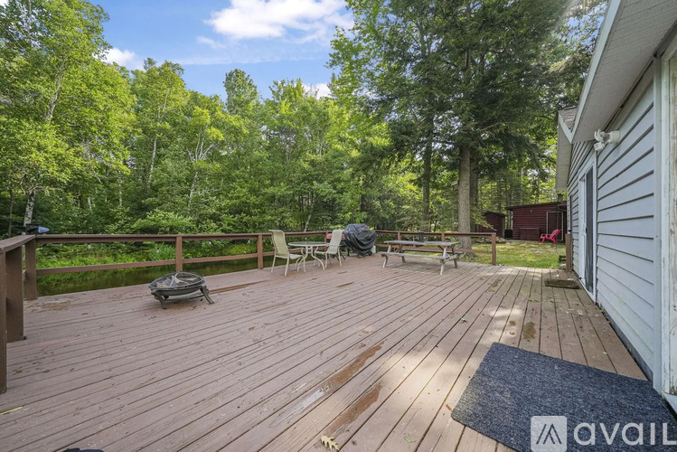 A wooden deck with a mat and chairs is surrounded by trees.