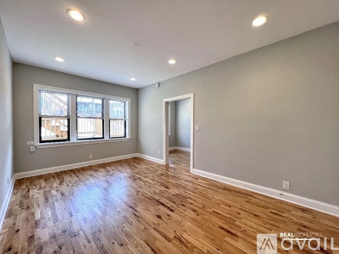 A spacious room with wooden flooring and a large window.