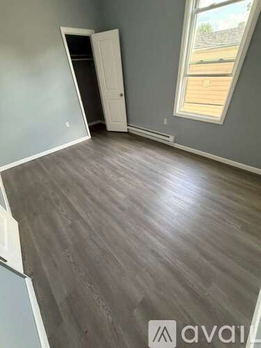 A room with grey flooring and a window showing a view of a backyard.