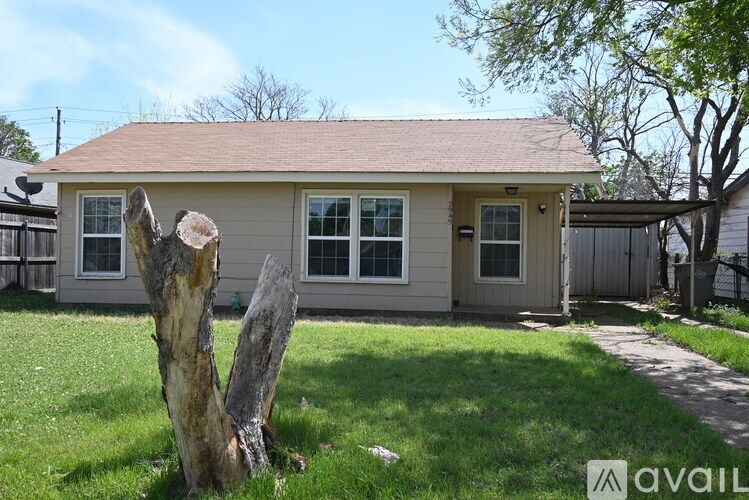 A house with a beige exterior and a brown roof is surrounded by a grassy lawn.