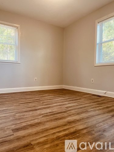 A room with wooden flooring and two windows.