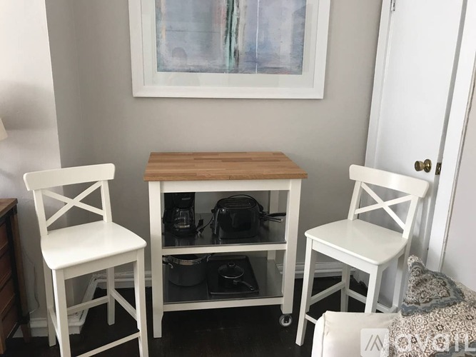 Two white chairs are placed in front of a small table with a coffee maker on it.
