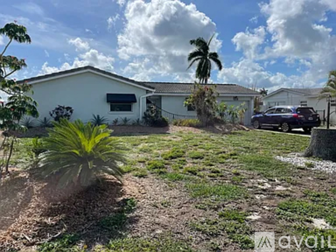 A white house with a car parked in front and a palm tree in the front yard.