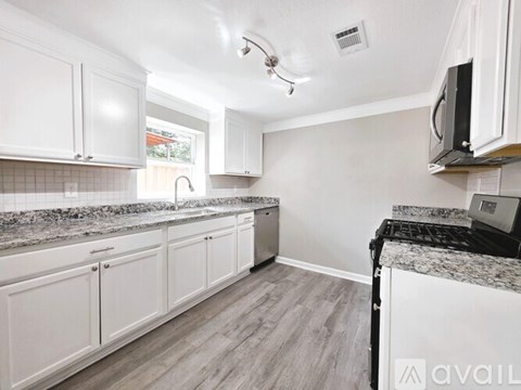 A kitchen with white cabinets and a black microwave.