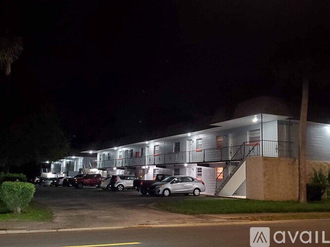 A parking lot with cars and a building with a lit up logo that says "AVAIL".