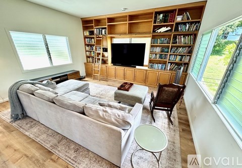 A living room with a large couch, a chair, a small table, and a bookshelf with a flat screen TV on top.