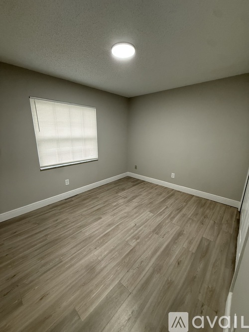 A room with wooden flooring and a window with blinds.