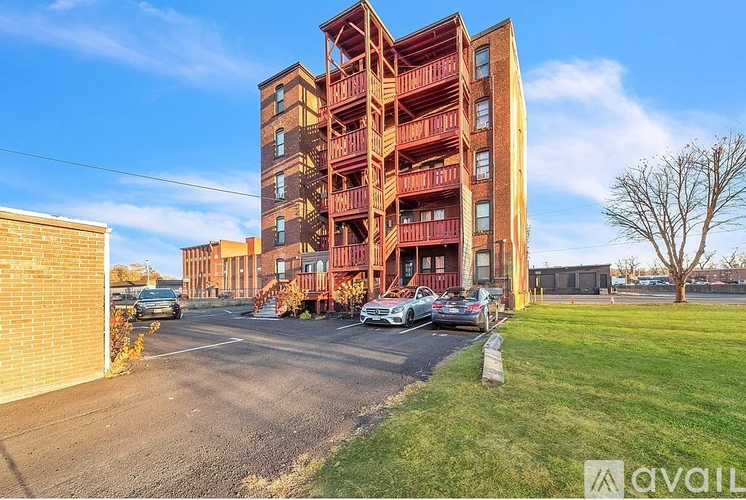A tall red brick apartment building with a parking lot in front.