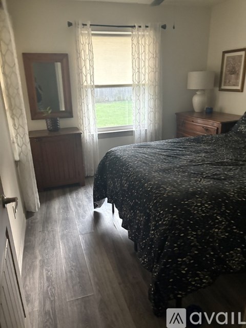 A bedroom with a large bed and a window with curtains.