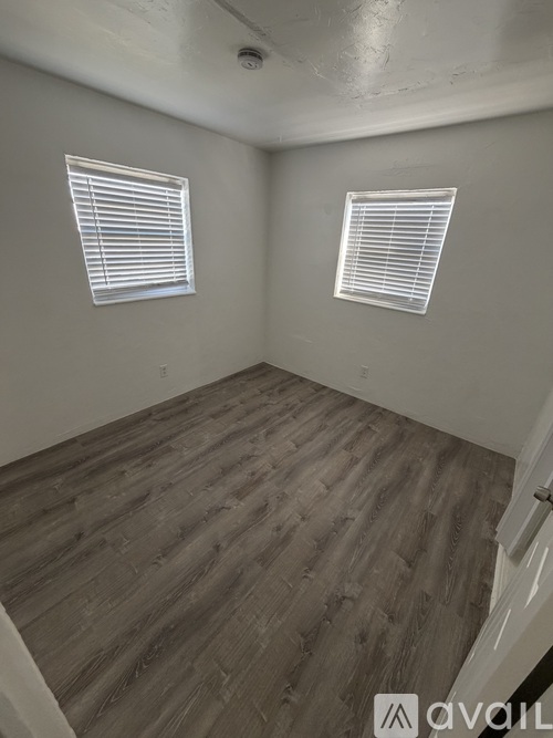 A room with wooden flooring and two windows.