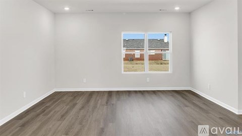 A spacious room with wooden flooring and a large window showing a view of a building outside.