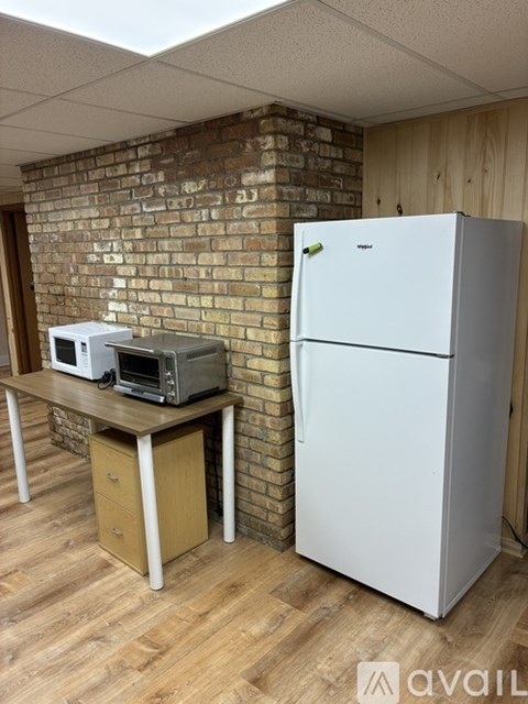 A white refrigerator stands next to a brick wall in a kitchen.