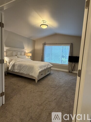 A bedroom with a large bed and a window with blinds.