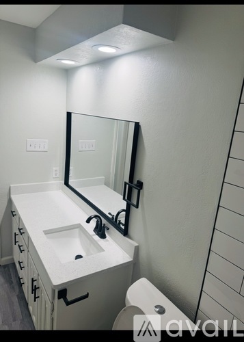A white bathroom with a sink, mirror, and toilet paper.