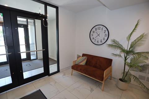 A living room with a sofa, a plant, and a clock on the wall.