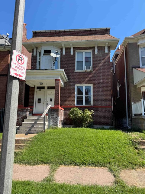 A red brick house with a white door and a sign on a pole in front of it.