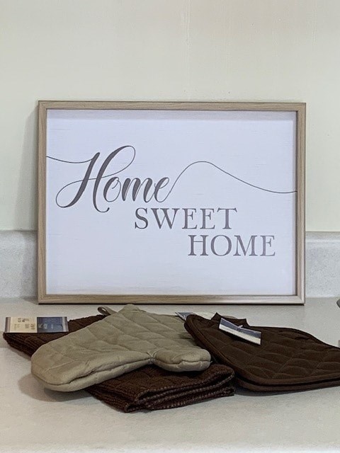 A framed sign that says "Home Sweet Home" is on a table with two blankets.
