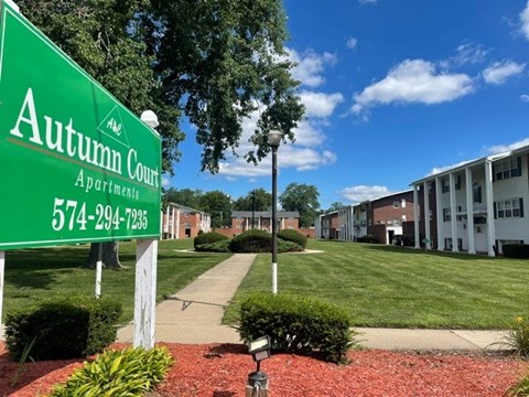 A green sign for Autumn Court Apartments stands in front of apartment buildings.