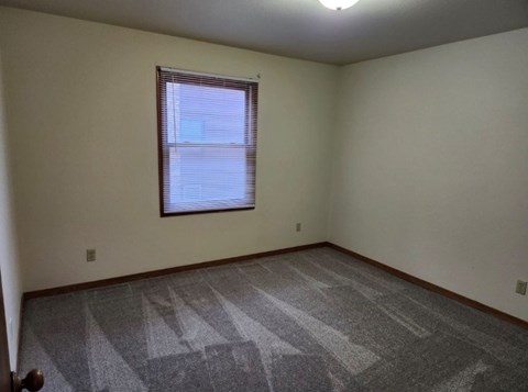 A room with a carpeted floor and a window with blinds.