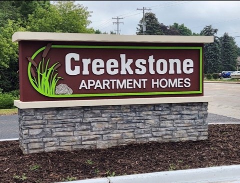 A sign for Creekstone Apartment Homes is displayed in front of a stone wall.