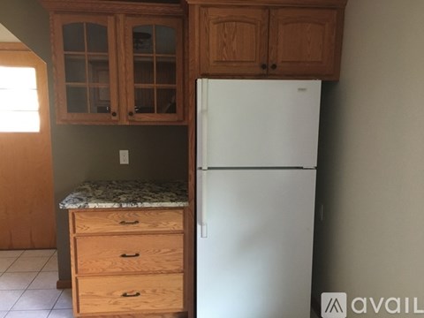 A white refrigerator stands next to wooden cabinets in a kitchen.
