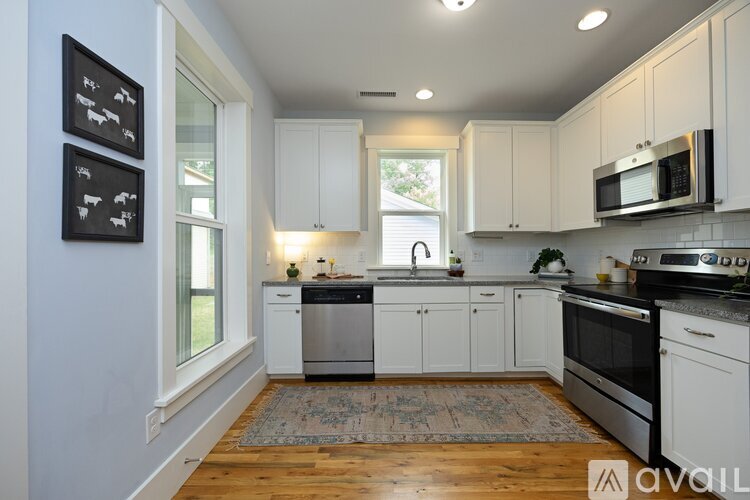 A kitchen with white cabinets and appliances, a rug on the floor, and pictures on the wall.