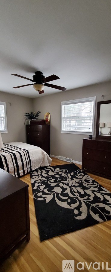 A bedroom with a ceiling fan and a rug on the floor.