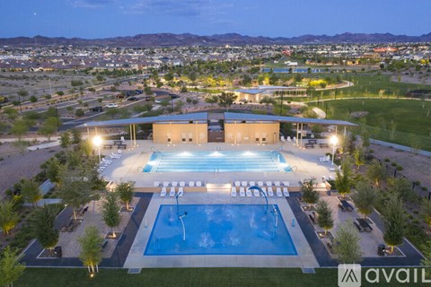 An aerial view of a swimming pool surrounded by a grassy area and buildings in the distance.
