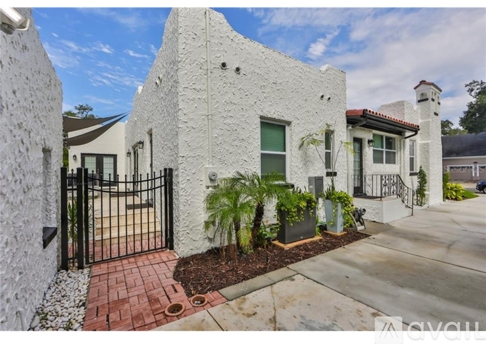 A white stucco house with a black gate and a brick pathway leading to the entrance.