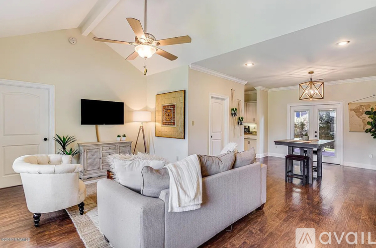 A living room with a grey couch, a white chair, a wooden floor, and a ceiling fan.