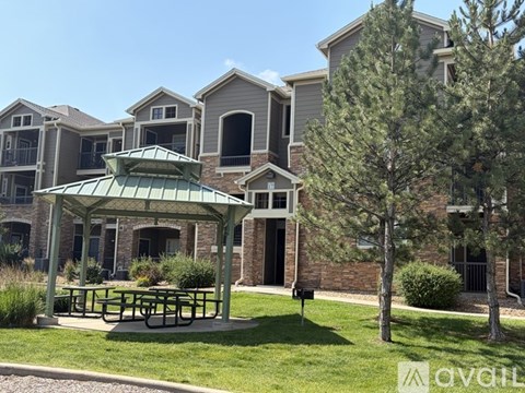 A patio with a table and chairs is surrounded by a grassy area and pine trees.