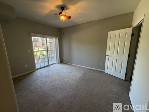 A spacious room with a ceiling fan and a sliding glass door leading to a balcony.