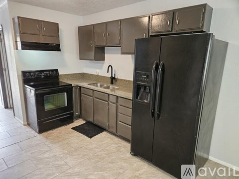 A kitchen with a black refrigerator, black oven, and brown cabinets.