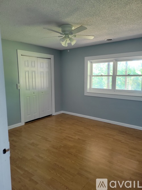 A room with a white door and a window with a ceiling fan.