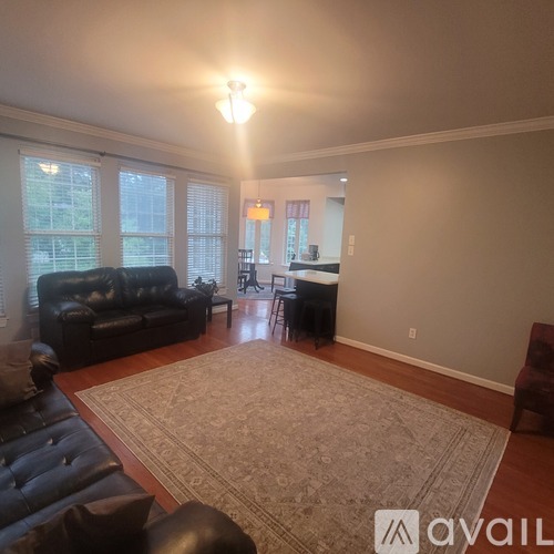 A living room with a black leather couch and a rug.