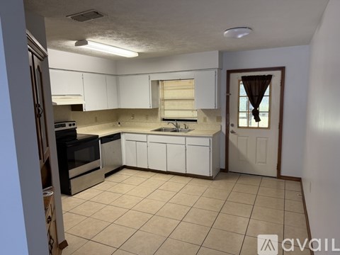 A kitchen with white cabinets and appliances, a window with curtains, and a door.