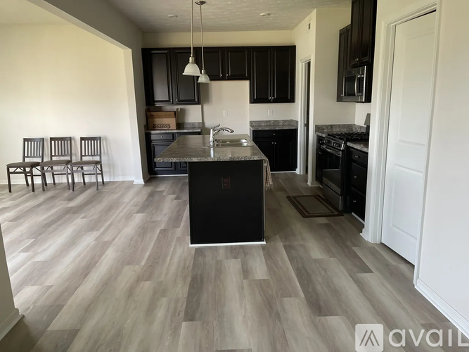 A kitchen with a black island in the middle of a room with wooden floors.