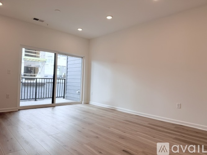 A spacious room with wooden floors and a sliding glass door leading to a balcony.