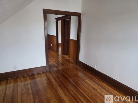 A room with wooden floors and a white wall with a doorway leading to another room.